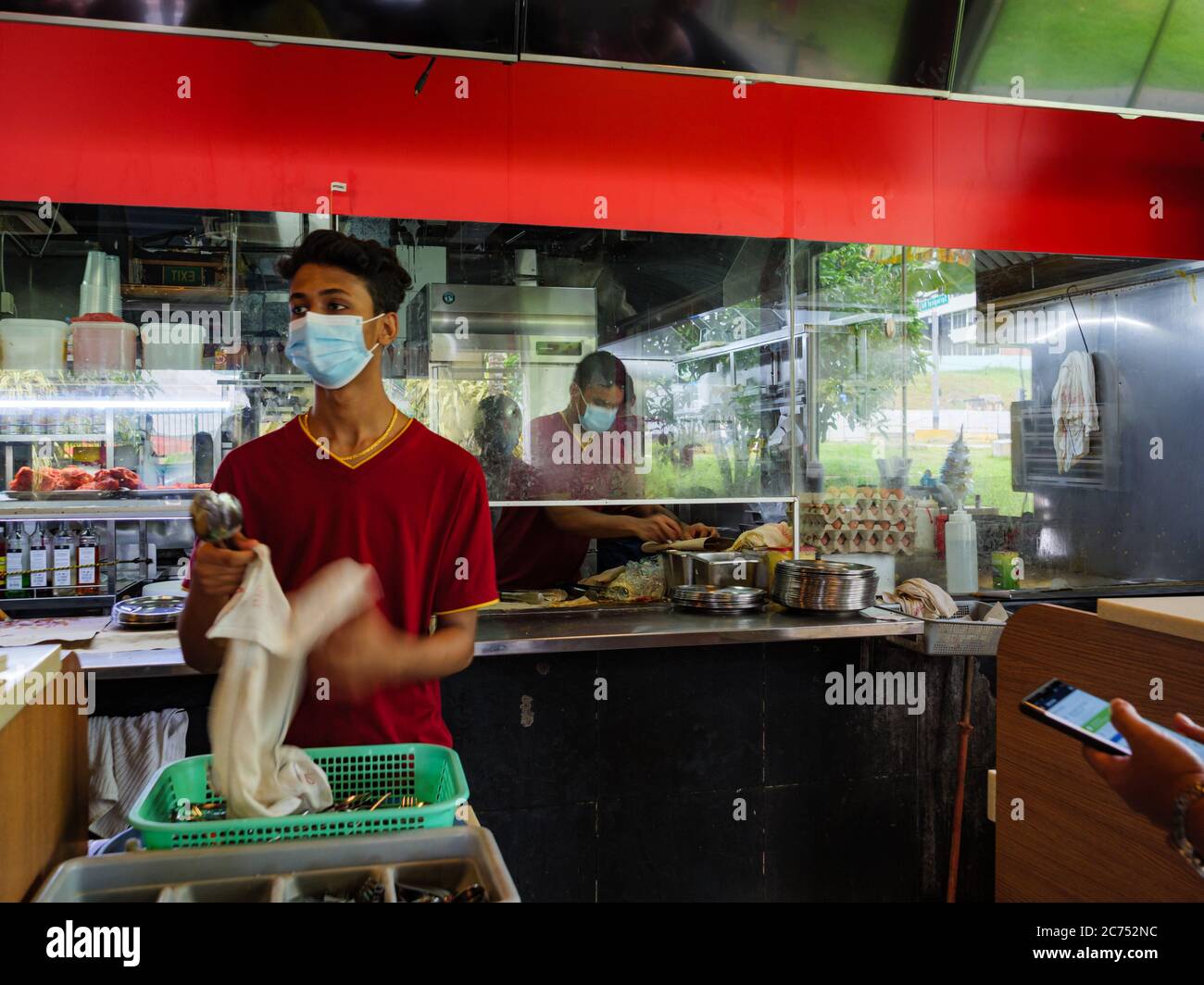 SINGAPORE – JULY 10 2020 – Employees at the Springleaf Prata Place Indian restaurant in Singapore wear protective masks as they clean cutlery and prep Stock Photo