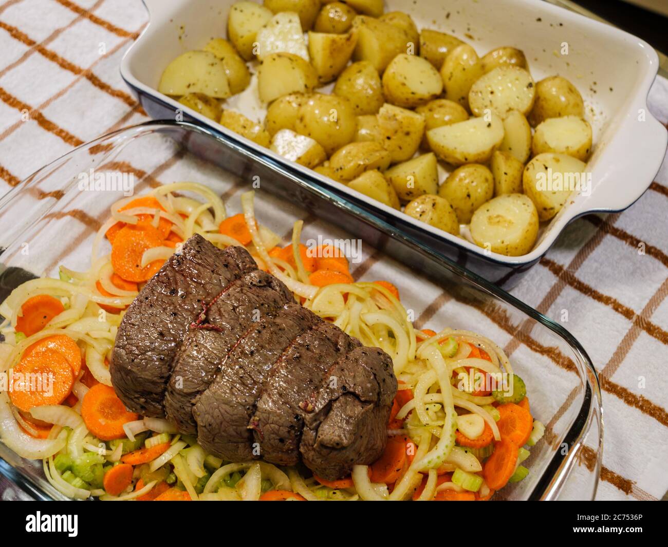 A traditional Sunday Roast meal of a topside roast beef and potatoes on a rustic checked tablecloth in a domestic kitchen Stock Photo