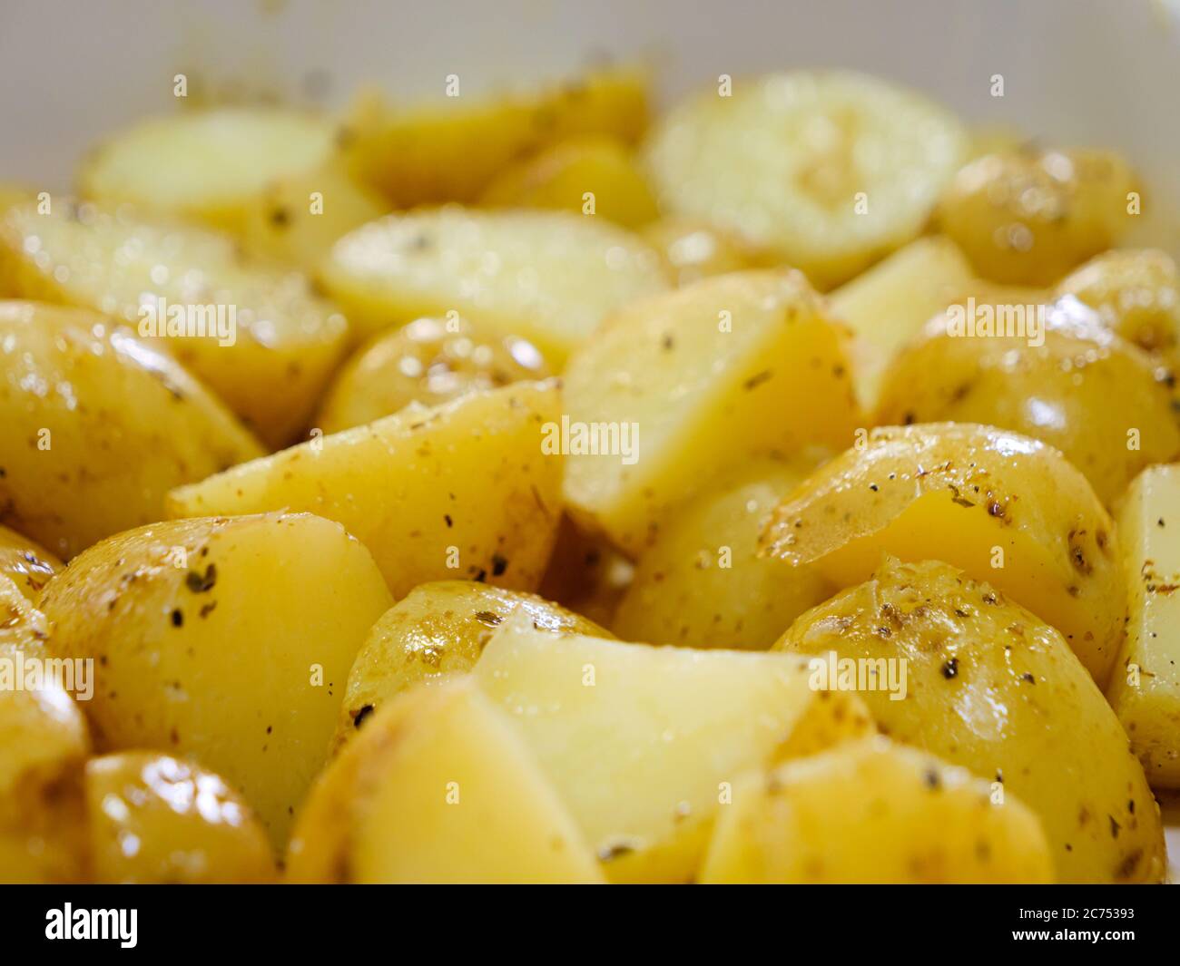 Macro close-up of sliced boiled potatoes seasoned with herbs and olive oil prior to being put in the oven Stock Photo