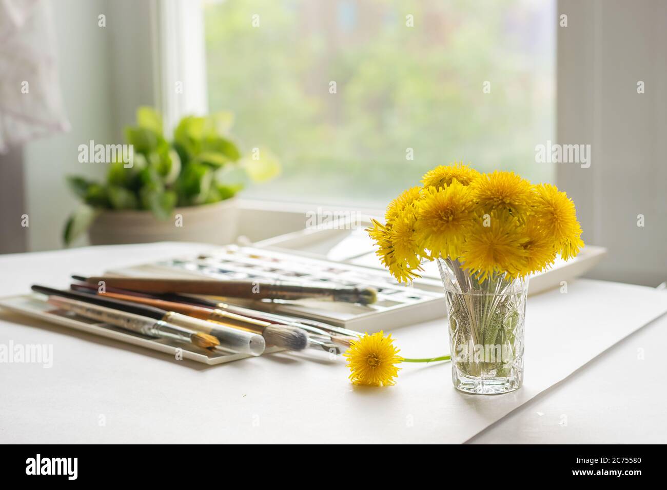 A bouquet of dandelions is on the table with paints and brushes for ...