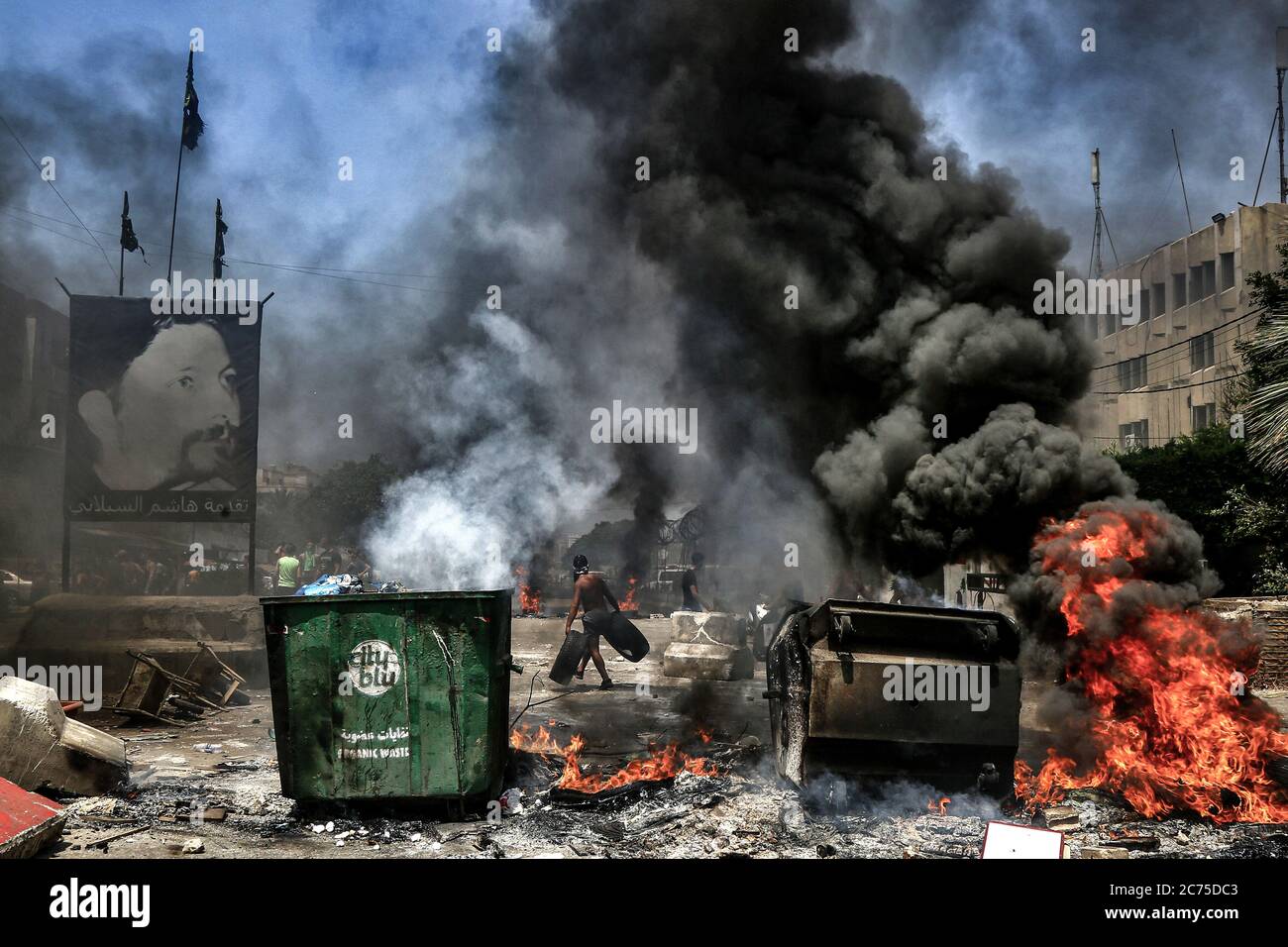 Beirut, Lebanon. 14th July, 2020. A demonstrator carries tyres on his way to burn them to block the main road in Ouzai, south of Beirut during an anti-government protest. Credit: Marwan Naamani/dpa/Alamy Live News Stock Photo