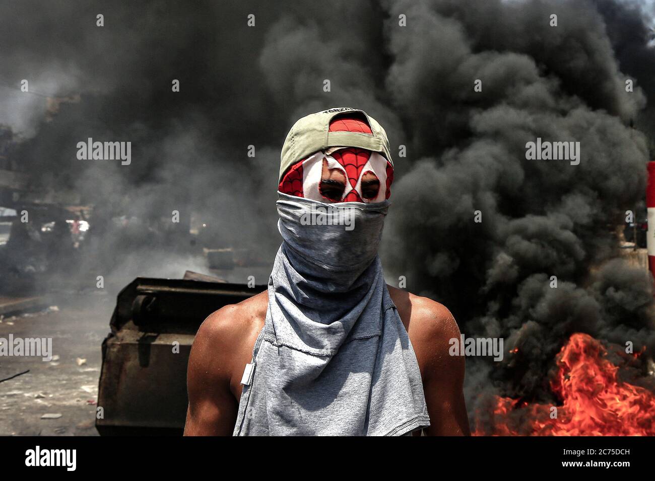 Beirut, Lebanon. 14th July, 2020. A masked demonstrator blocks the main road in Ouzai, south of Beirut by burning tyres during an anti-government protest. Credit: Marwan Naamani/dpa/Alamy Live News Stock Photo