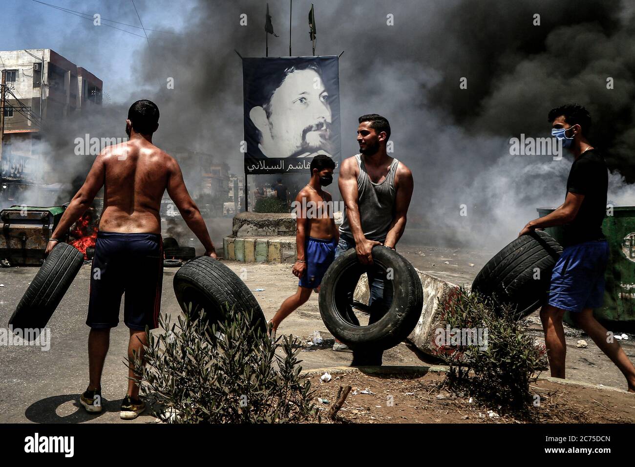 Beirut, Lebanon. 14th July, 2020. Demonstrators carry tyres to burn them and to block the main road in Ouzai, south of Beirut during an anti-government protest. Credit: Marwan Naamani/dpa/Alamy Live News Stock Photo