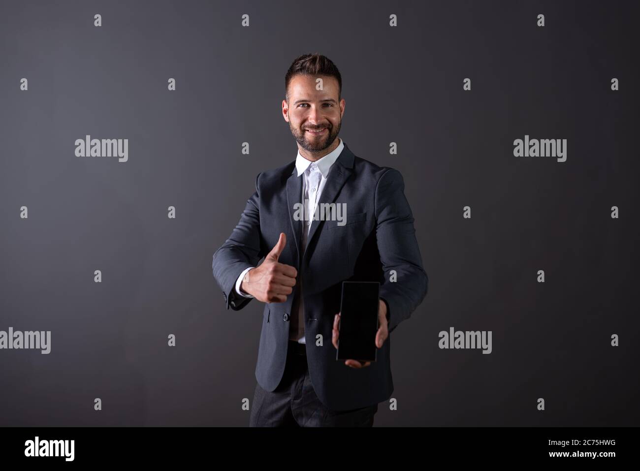 A smiling handsome young businessman in a suit showing the screen of a ...