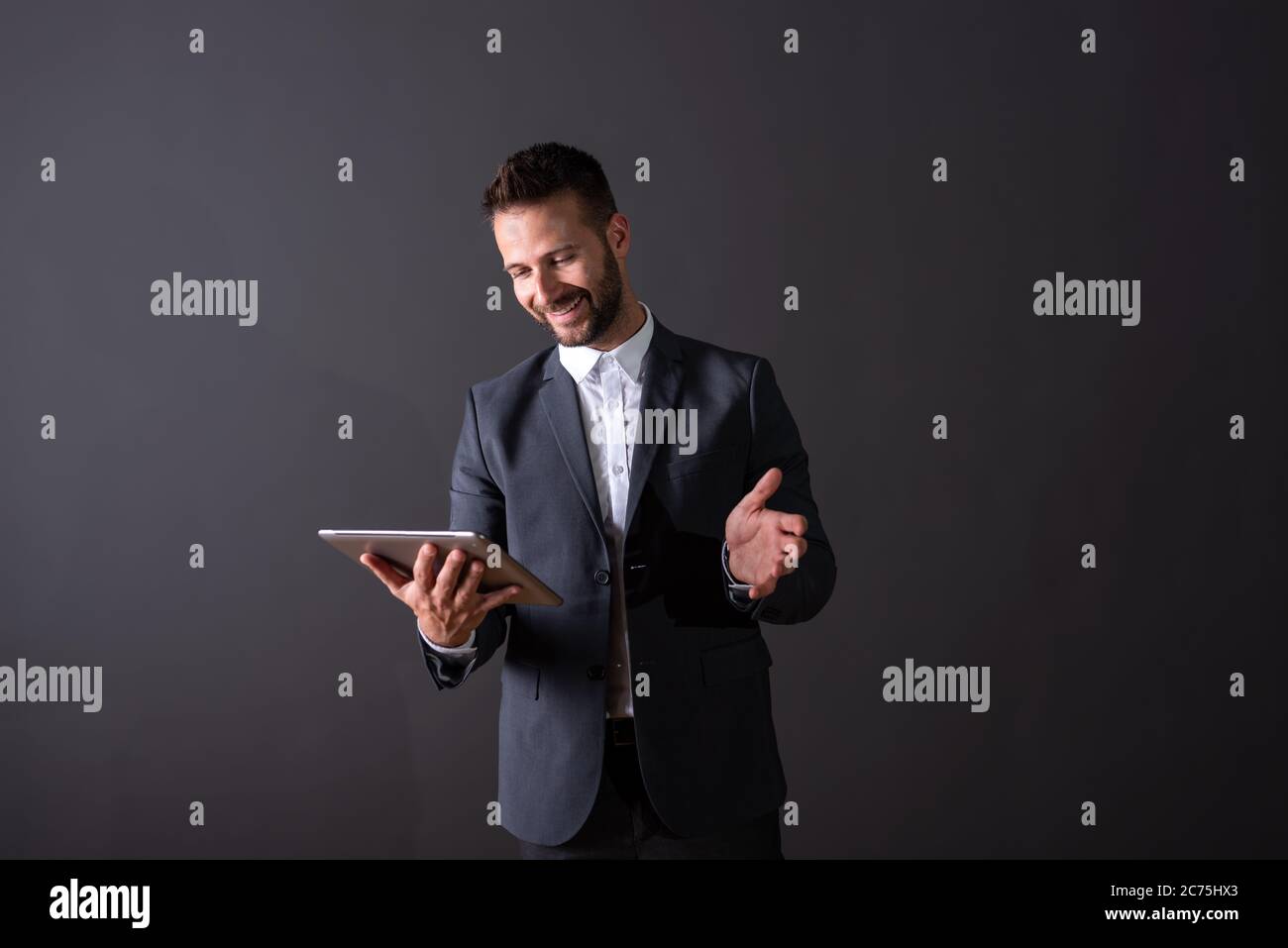 A smiling handsome young businessman in a suit using a tablet in front ...