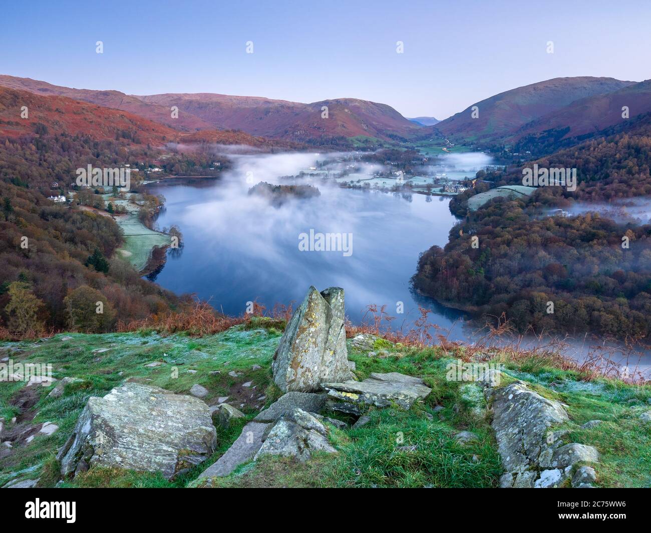 Dawn light turns the fells overlooking Grasmere (The Lake District) red as mist starts to fill the frosty valley on a completely clear autumn morning. Stock Photo
