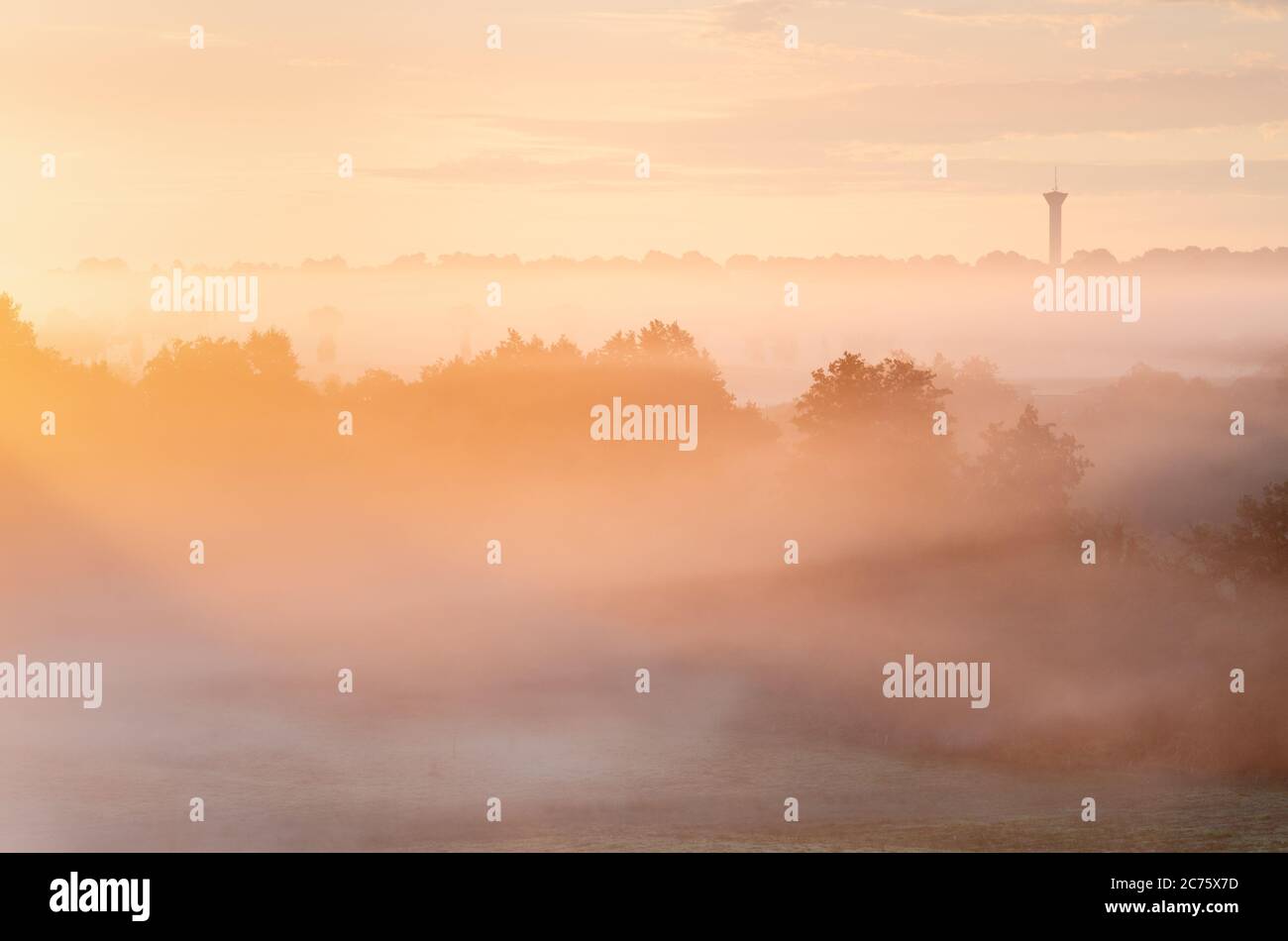 The first direct light from the sun lights up the misty landscape of Poitou Charentes in France, with a traditional water tower visible on the horizon. Stock Photo