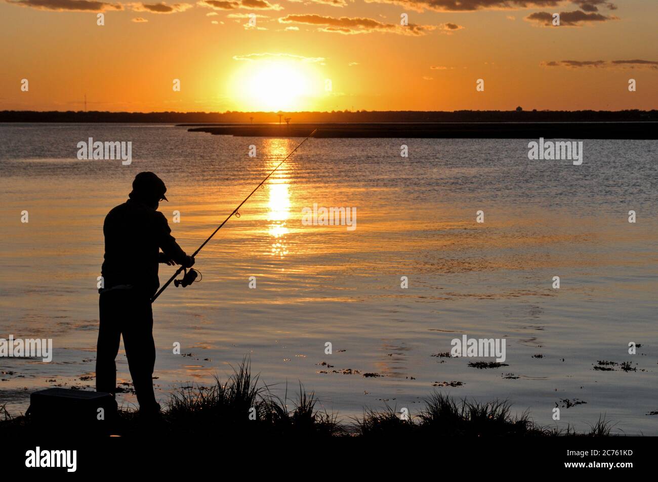 A man is fishing on the lake against the backdrop of sunset. The