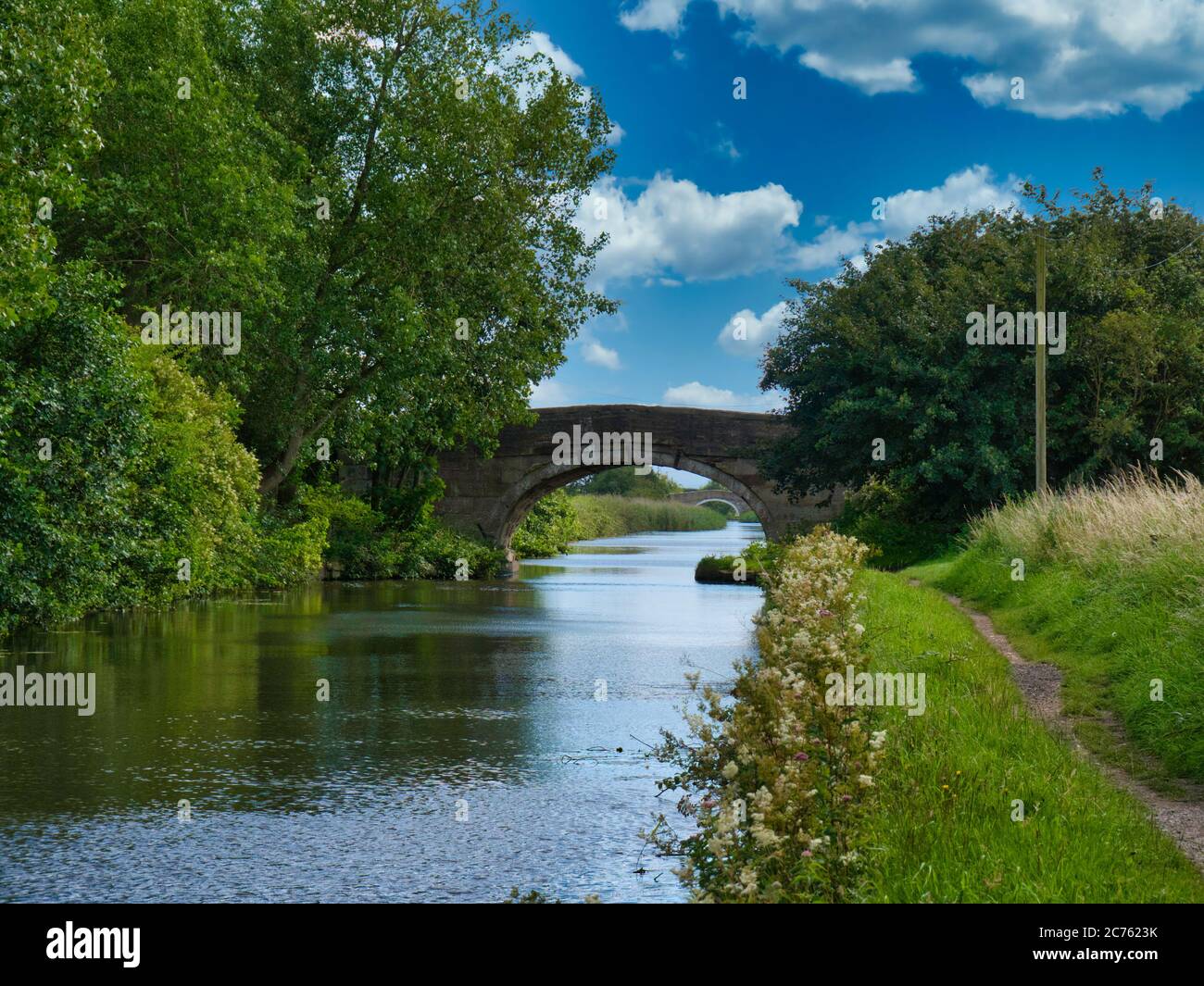 Two bridges on a quiet, rural section of the Leeds to Liverpool Canal in Lancashire, UK. Taken on a sunny day with blue sky and white clouds in summer Stock Photo