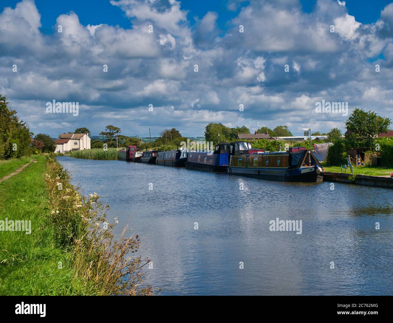 A row of canal narrowboats moored at permanent moorings on a quiet, rural stretch of the Leeds to Liverpool Canal in Lancashire, taken on a sunny day Stock Photo