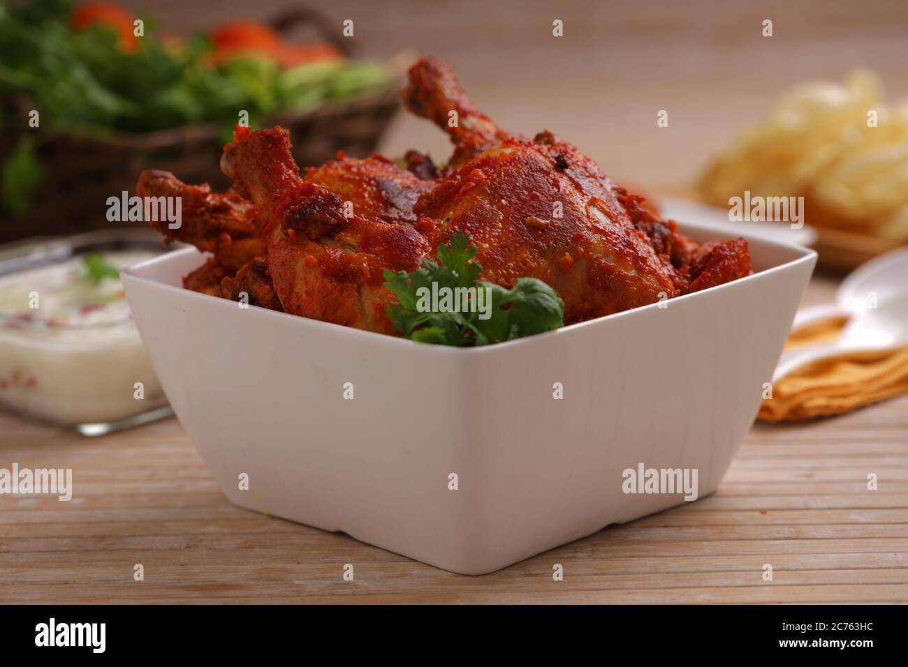 Spicy Tandoori chicken garnished with lemon and coriander leaf in square shaped white bowl with wooden background,selective focus Stock Photo