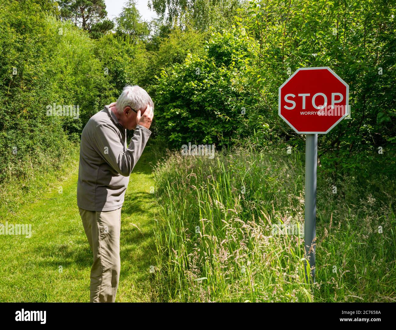 Quirky Stop Worrying warning sign on country path with senior man looking worried, Gifford, East Lothian, Scotland, UK Stock Photo