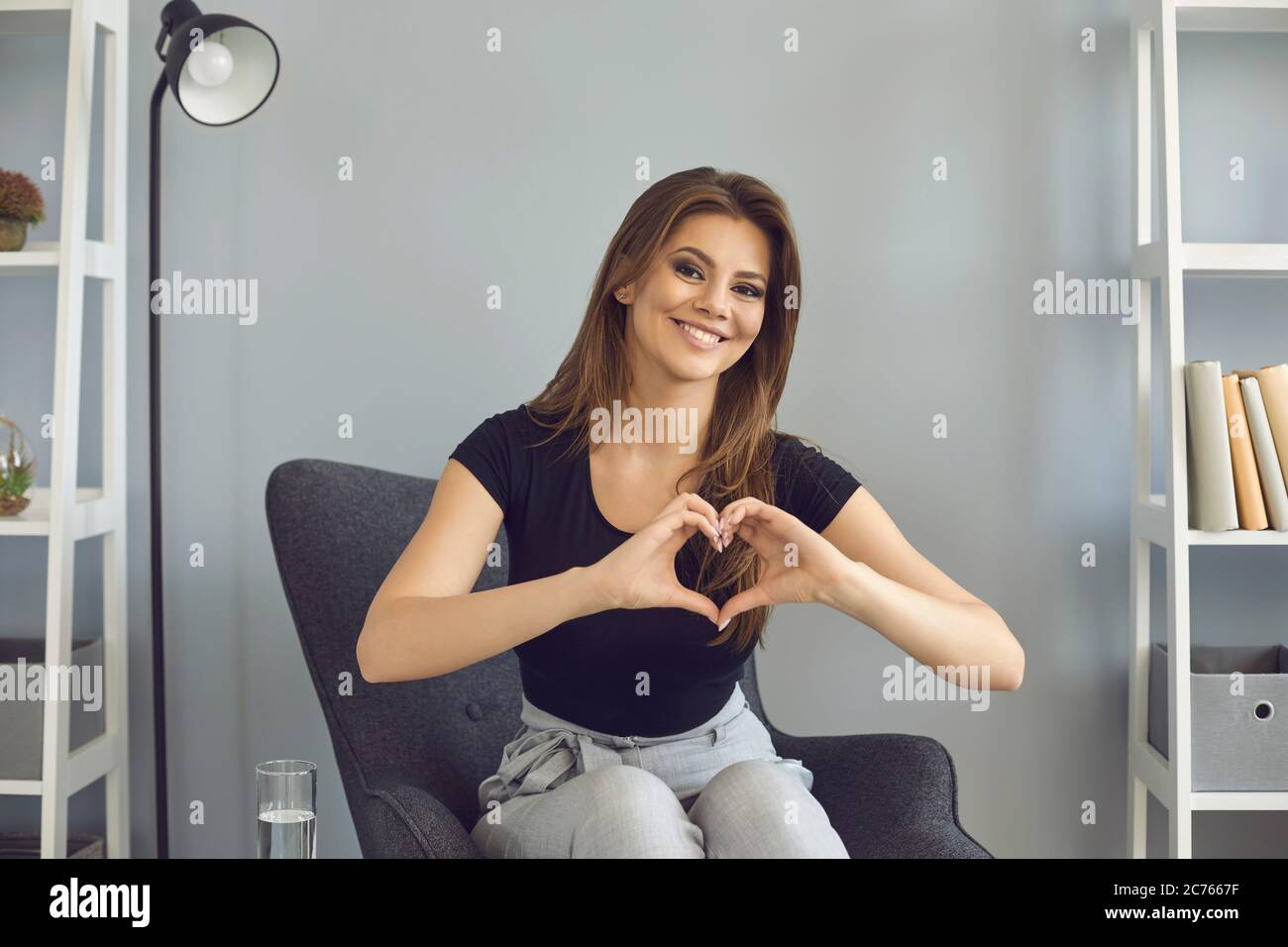 Online dating concept. Romantic young woman showing heart with hands during web conference with her boyfriend indoors Stock Photo