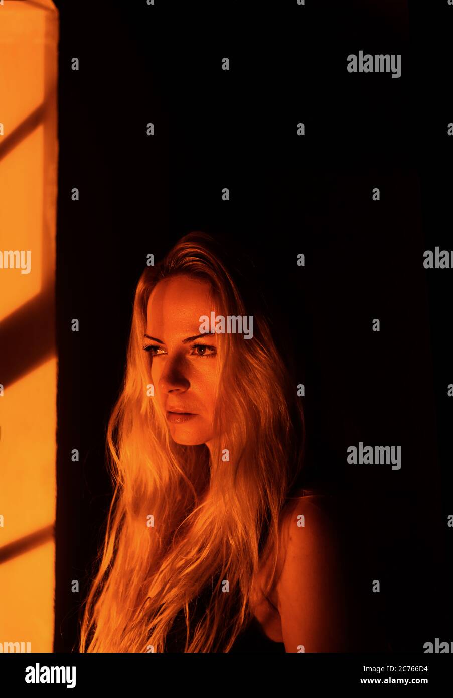 woman with long blond hair standing by a window at night Stock Photo