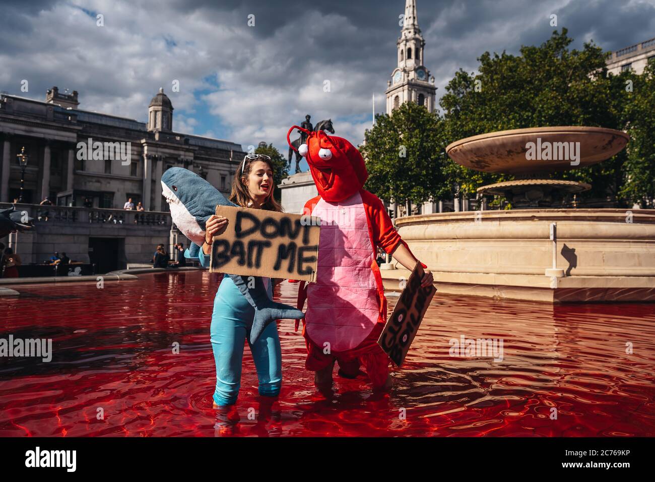 London / UK - 07/11/2020: couple wearing costumes and holding banners standing in the fountain after animal rights group turns fountains water red in Stock Photo