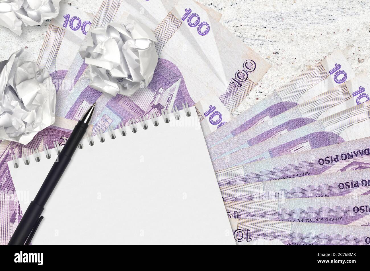 100 Philippine piso bills and balls of crumpled paper with notepad. Bad ideas or less of inspiration concept. Searching ideas for investment Stock Photo