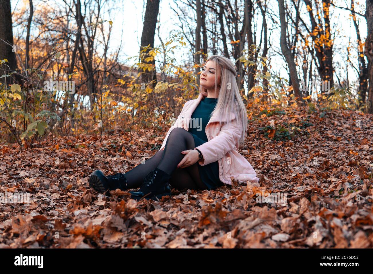 A young pleasant woman in casual clothes with long hair is sitting in the autumn forest. Stock Photo