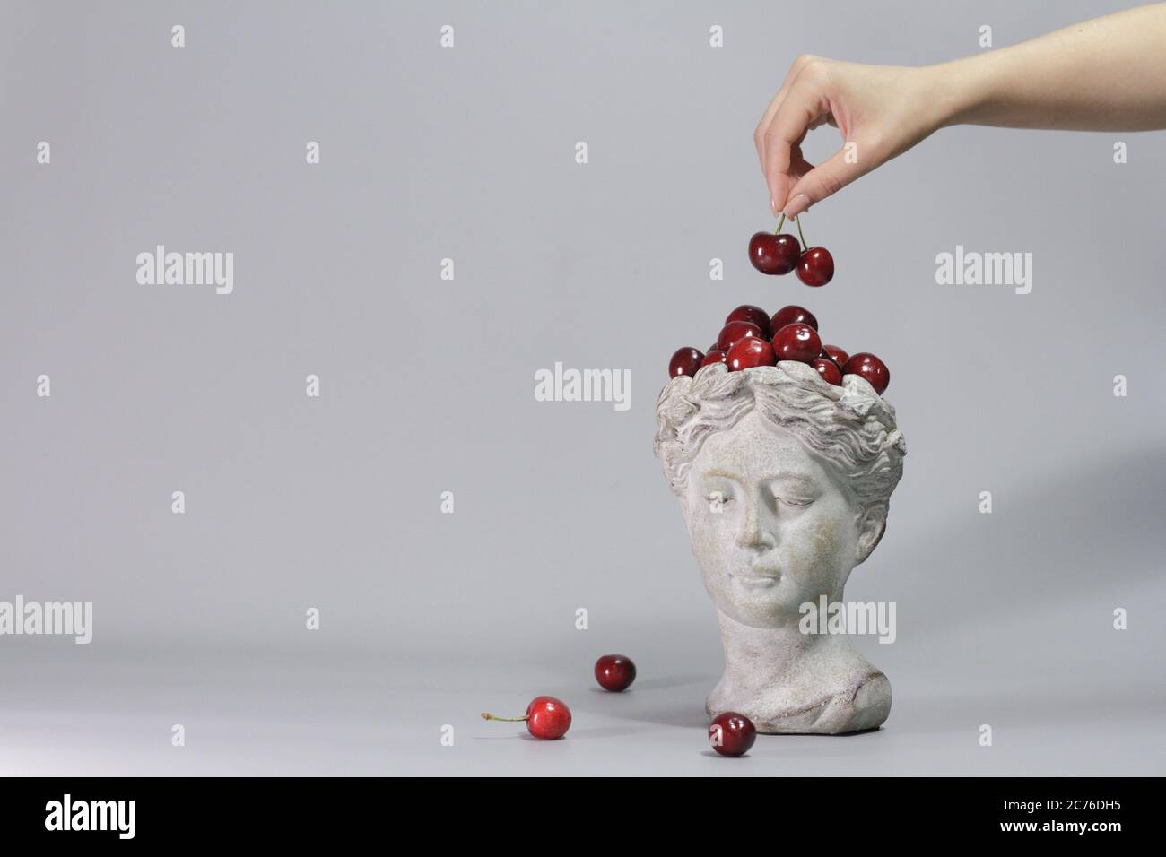 Stylish decoration made in shape of Greek goddess head full of red ripe cherries. Beautiful design elements. Gray background. Stock Photo