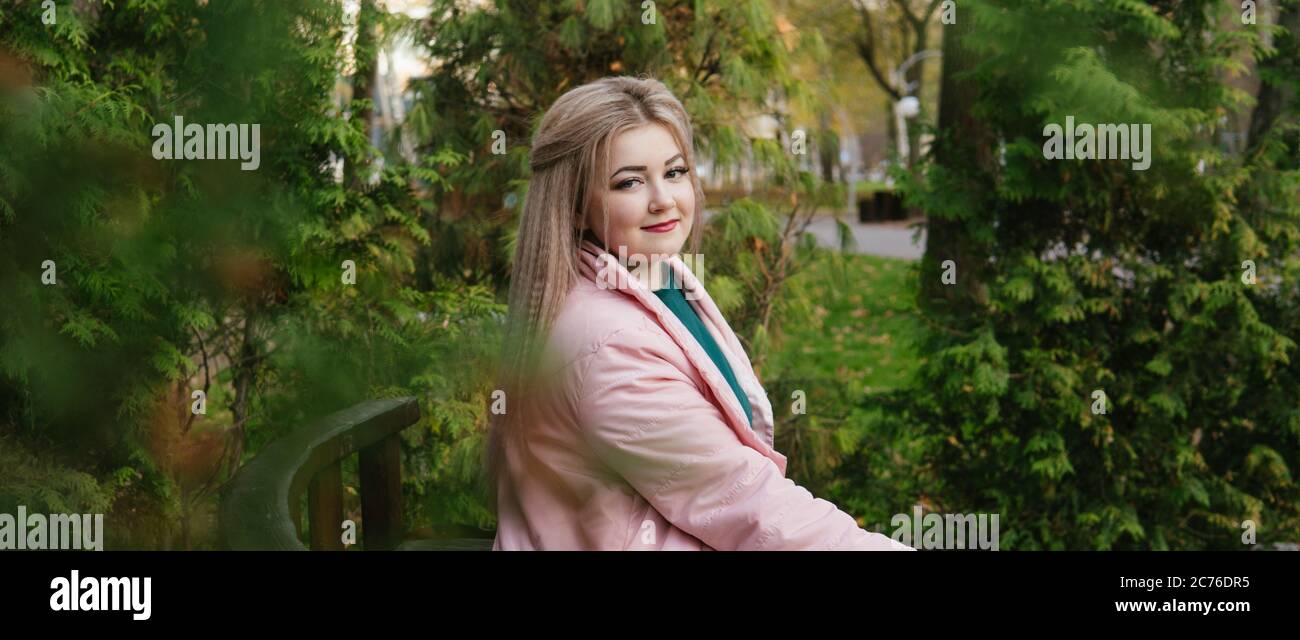 A portrait of a beautiful woman, sitting on a bench near the green vegetation. Stock Photo