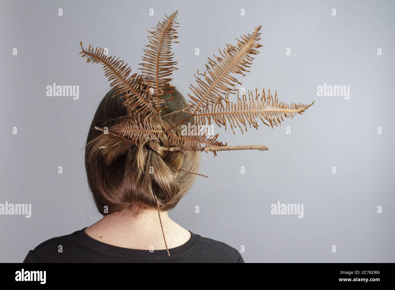 Rear view portrait of brunette girl with crown of fern in her hair, gray background. Stylish Hairstyle with Golden Umbrella Fern. Stock Photo