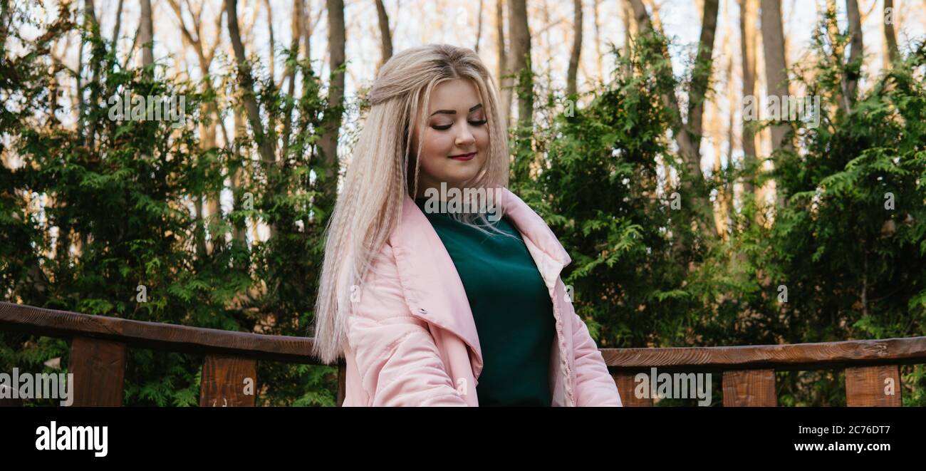 A portrait of a beautiful woman, sitting on a bench near the green vegetation. Stock Photo