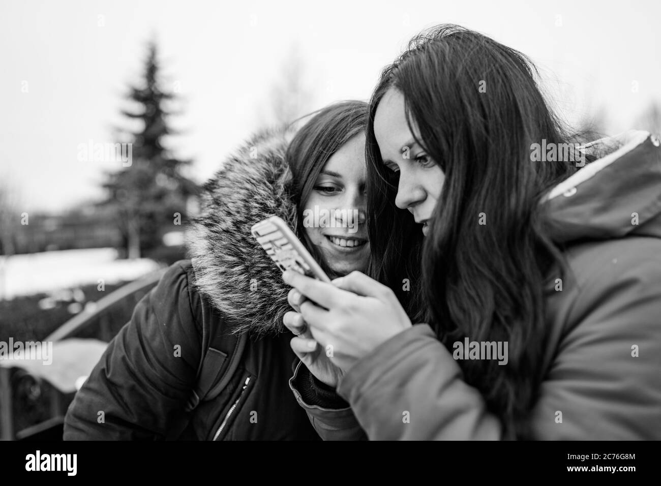 The meeting of girlfriends on street. Two women look in mobile phone, considering their photos on walk. Black and white photo. Stock Photo