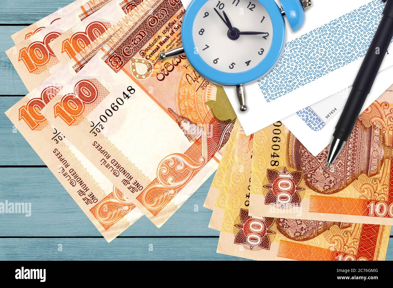 100 Sri Lankan rupees bills and alarm clock with pen and envelopes. Tax