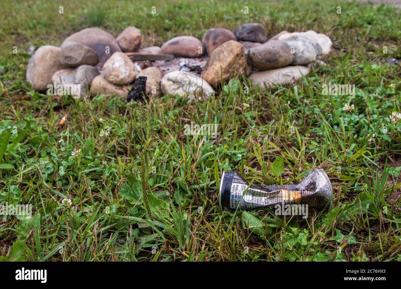 A discarded beer can left on the ground beside a campfire stone ring on a camping site, Leave No Trace habits Stock Photo
