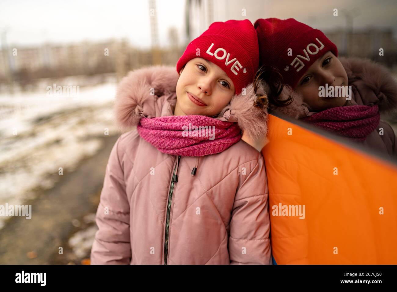 Portrait of charming little girl, posing near transport. Child in casual clothes on walk in winter season. Stock Photo