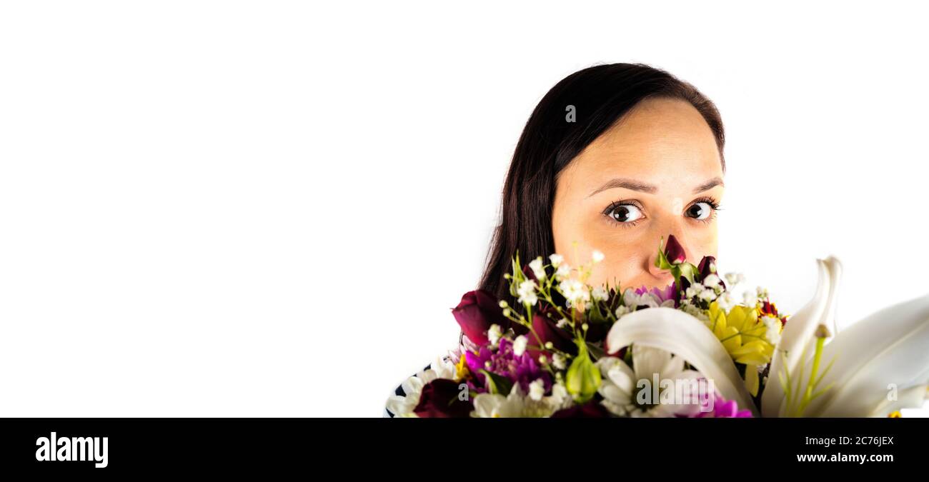 Young woman with colorful bouquet of various flowers on isolated white background. Brunette looks out from behind basket of florets. Stock Photo