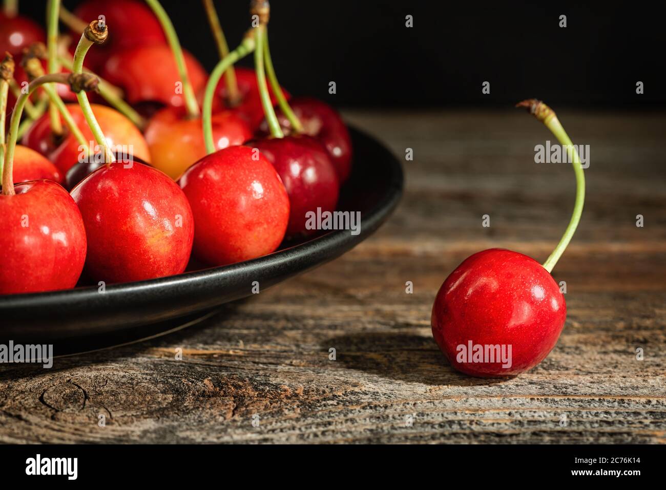 Sweet cherries on a plate on a wooden surface. Low key. Stock Photo
