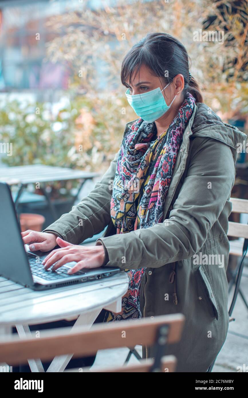 woman sitting in empty cafe wearing protecting mask working on laptop ...