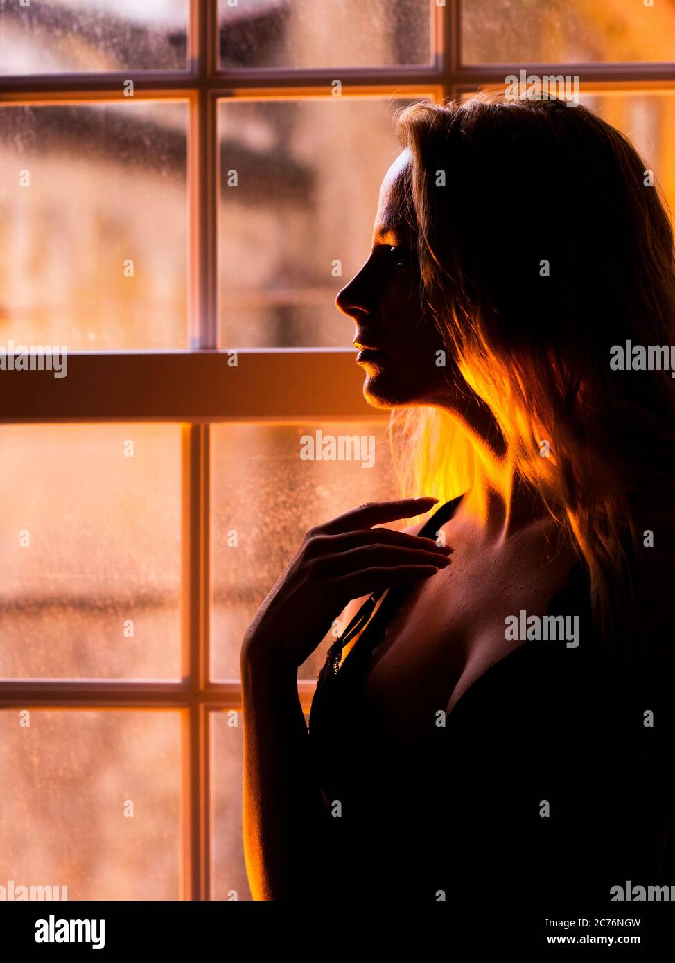 woman with long hair standing by a window at night Stock Photo