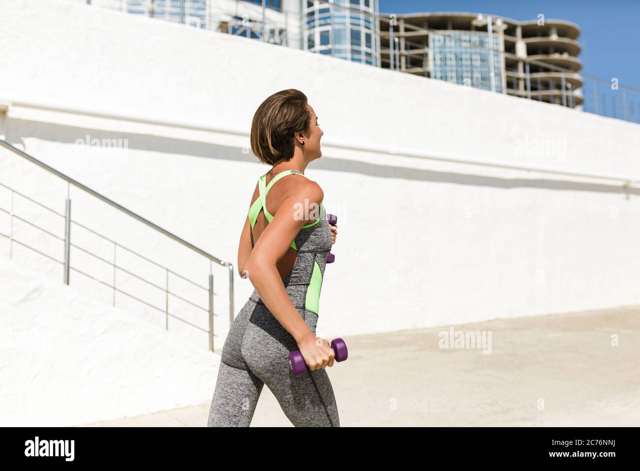 Beautiful woman with short hair in modern gray sport suit holding dumbbells in hands while jogging Stock Photo