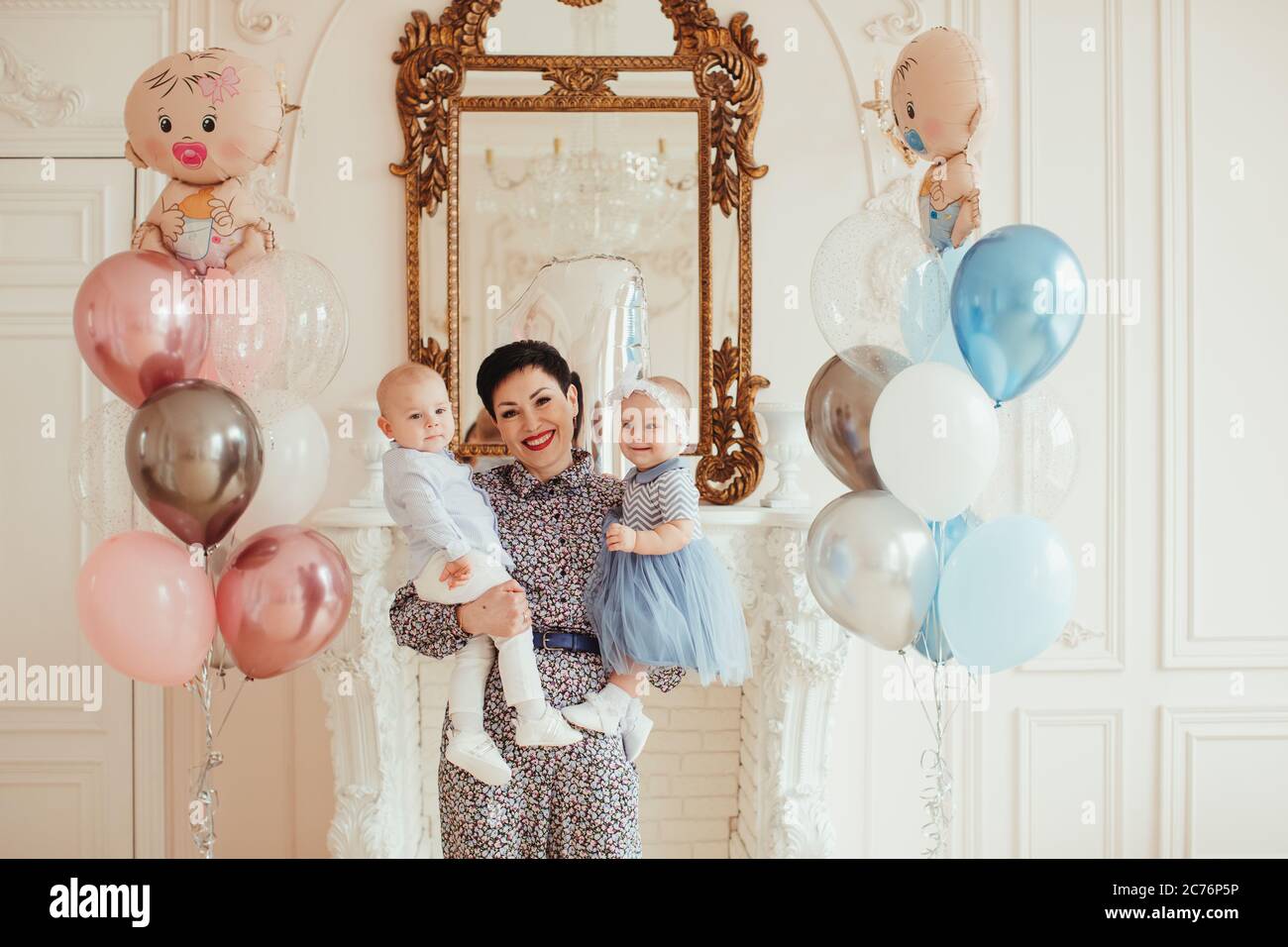 Portrait of a smiling woman holding her twin grandchildren on their 1st birthday Stock Photo