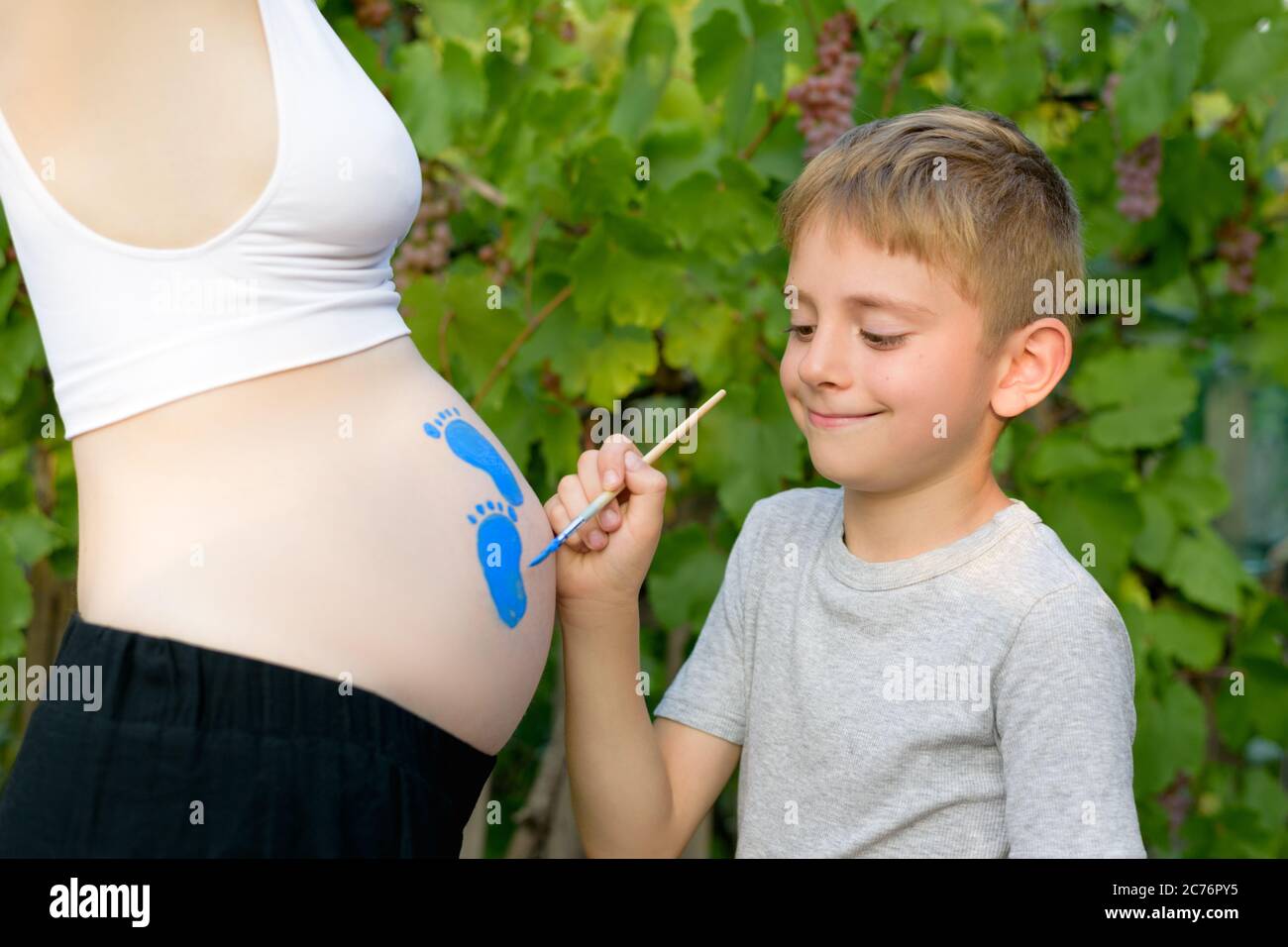 Little boy draws with a brush on the belly of his pregnant mom baby's