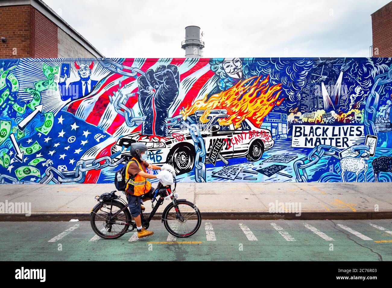Brooklyn, New York, USA - June 27, 2020: Bicycle delivery man rides past Painted mural depicting the Black Lives Matter and covid-19 in New York. Stock Photo