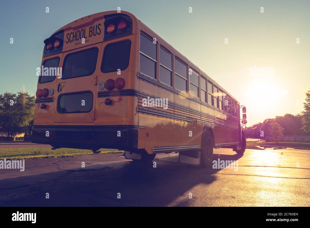 Back right low angle view of American Public school bus driving away with sunset in the distance Stock Photo