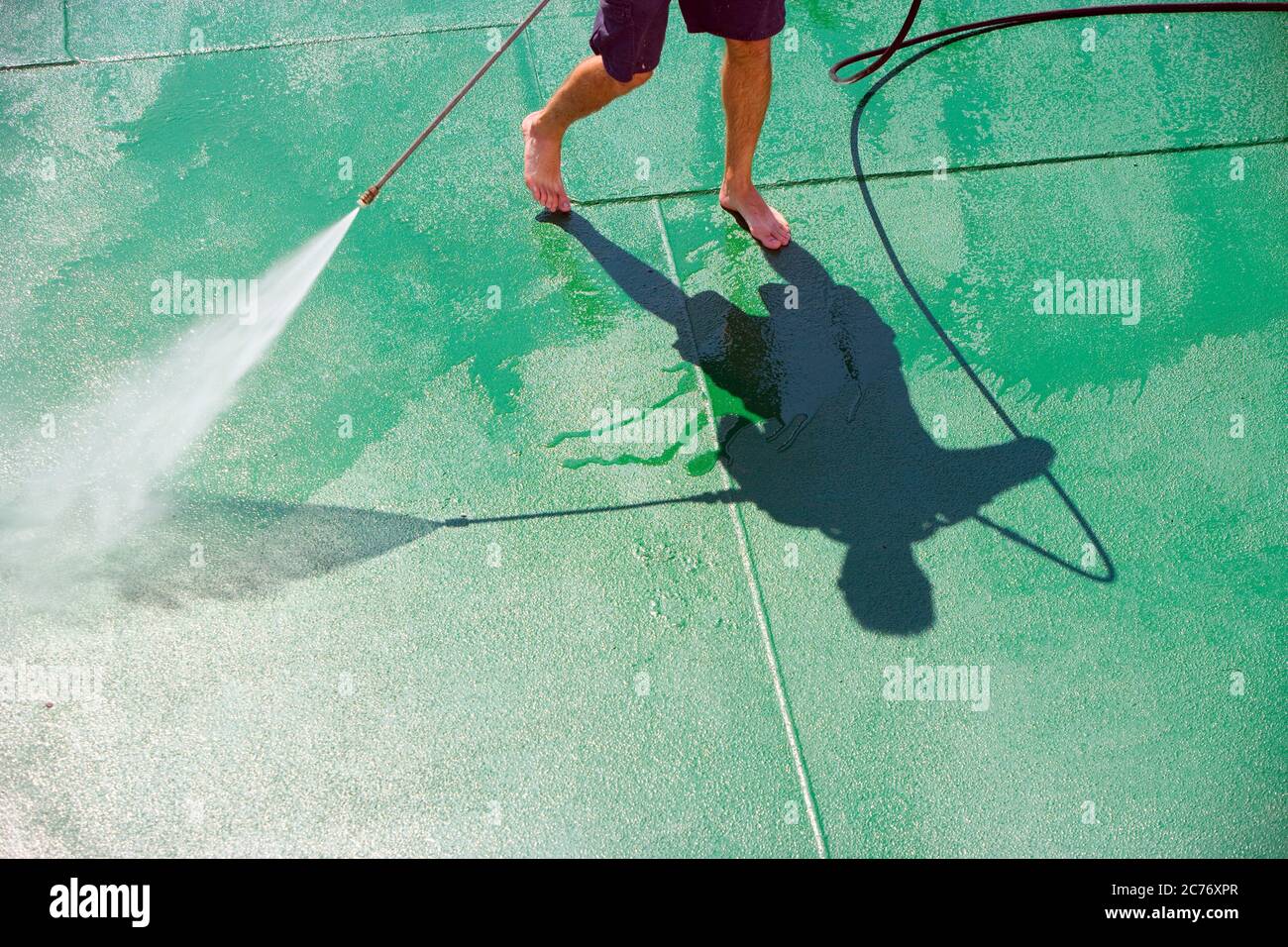 Shadow of a deckhand seen from above as he hoses down the steel deck of a ferry boat Stock Photo