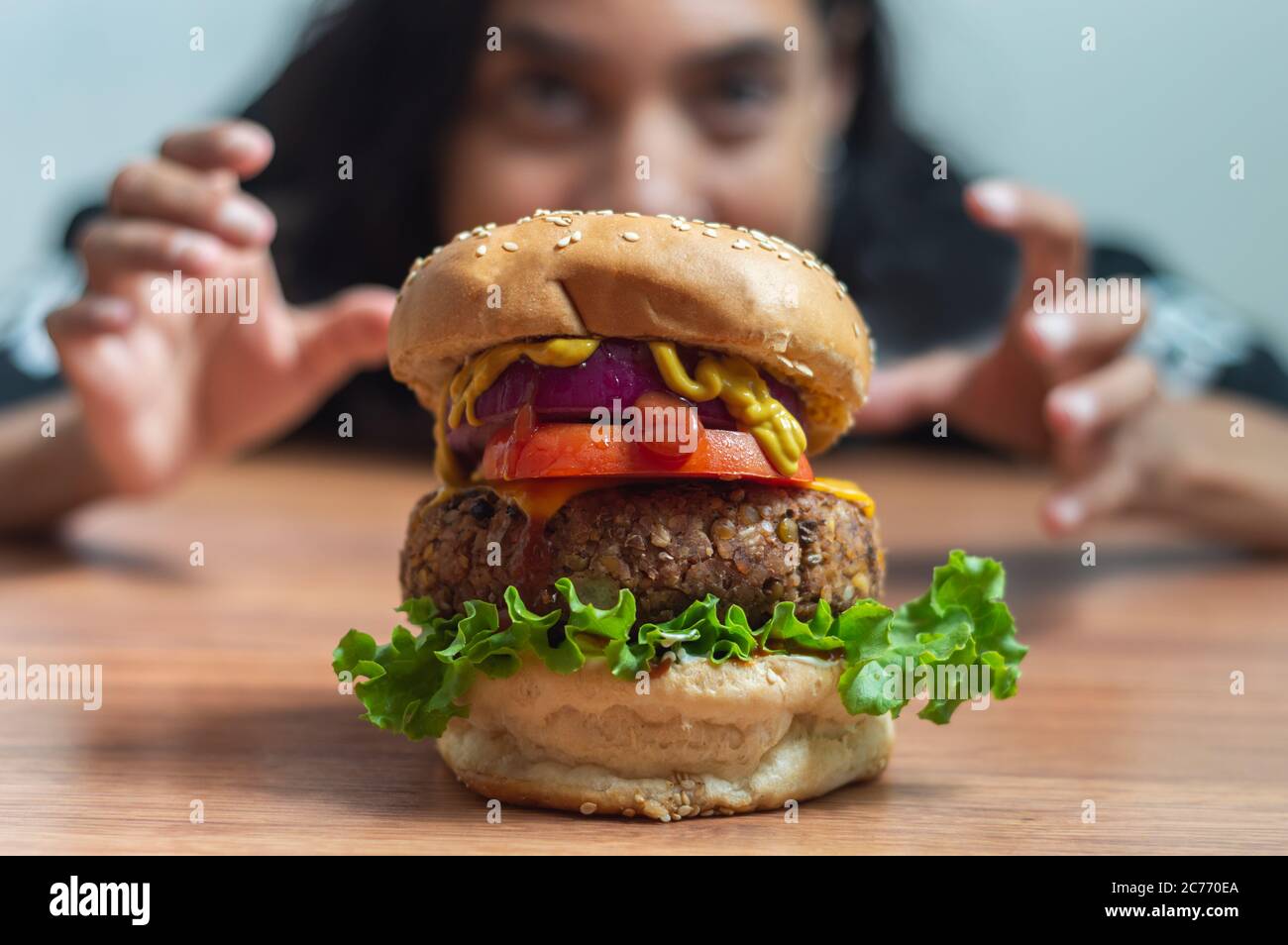 Pretty Mexican girl staring in surprise and grabbing at large vegetarian burger made of beans and lentils Stock Photo