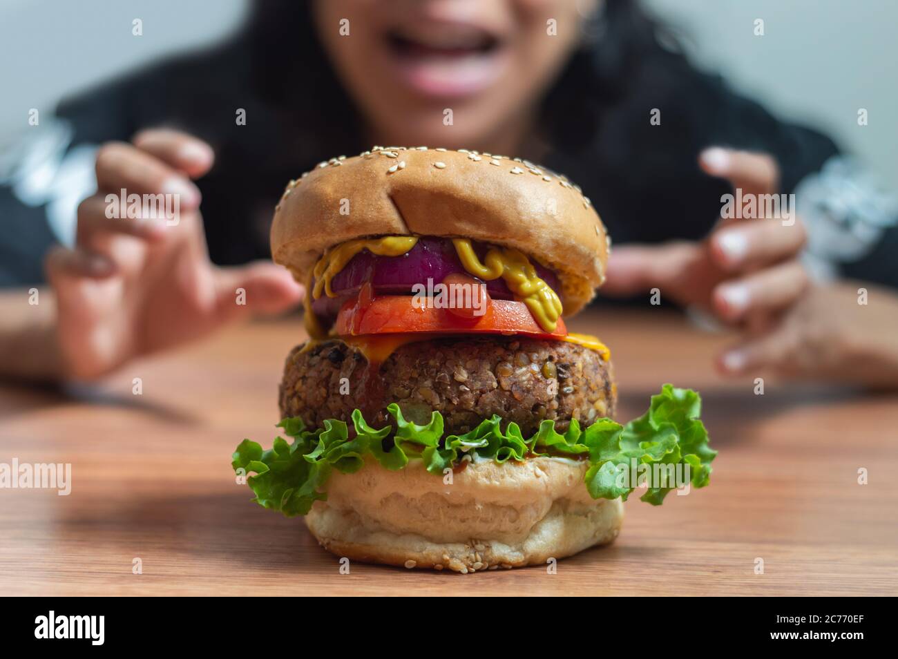 Pretty Mexican girl staring in surprise and grabbing at large vegetarian burger made of beans and lentils Stock Photo