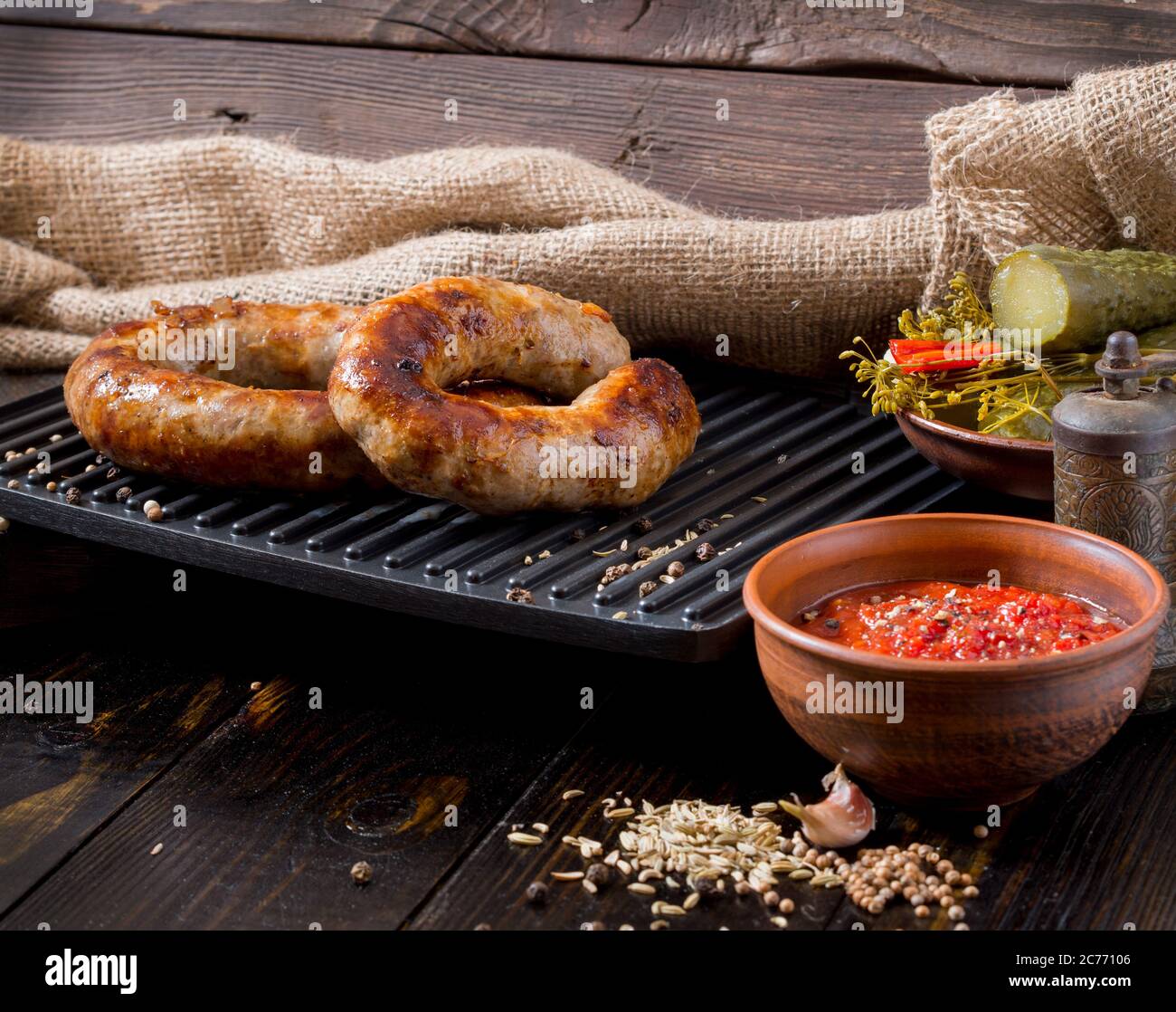 Spicy homemade sausages pork and beef sausages, on a wooden background, with sauce,  spices and pickled cucumber . Template in rustic style. Stock Photo