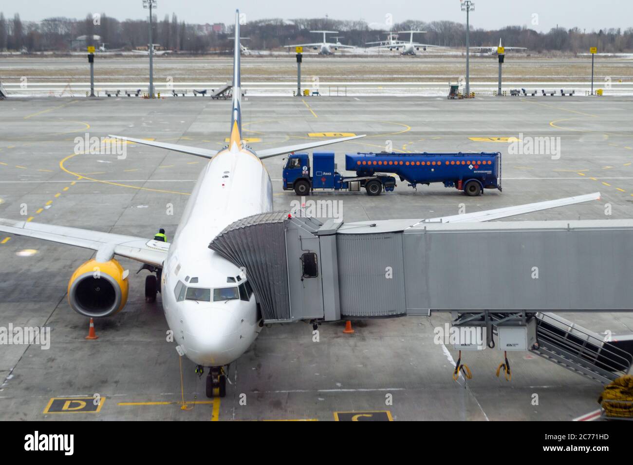 plane with jet bridge connected, blue gas tank with word flammable carries fuel to airplane. air plane at parking place. runway view. Stock Photo