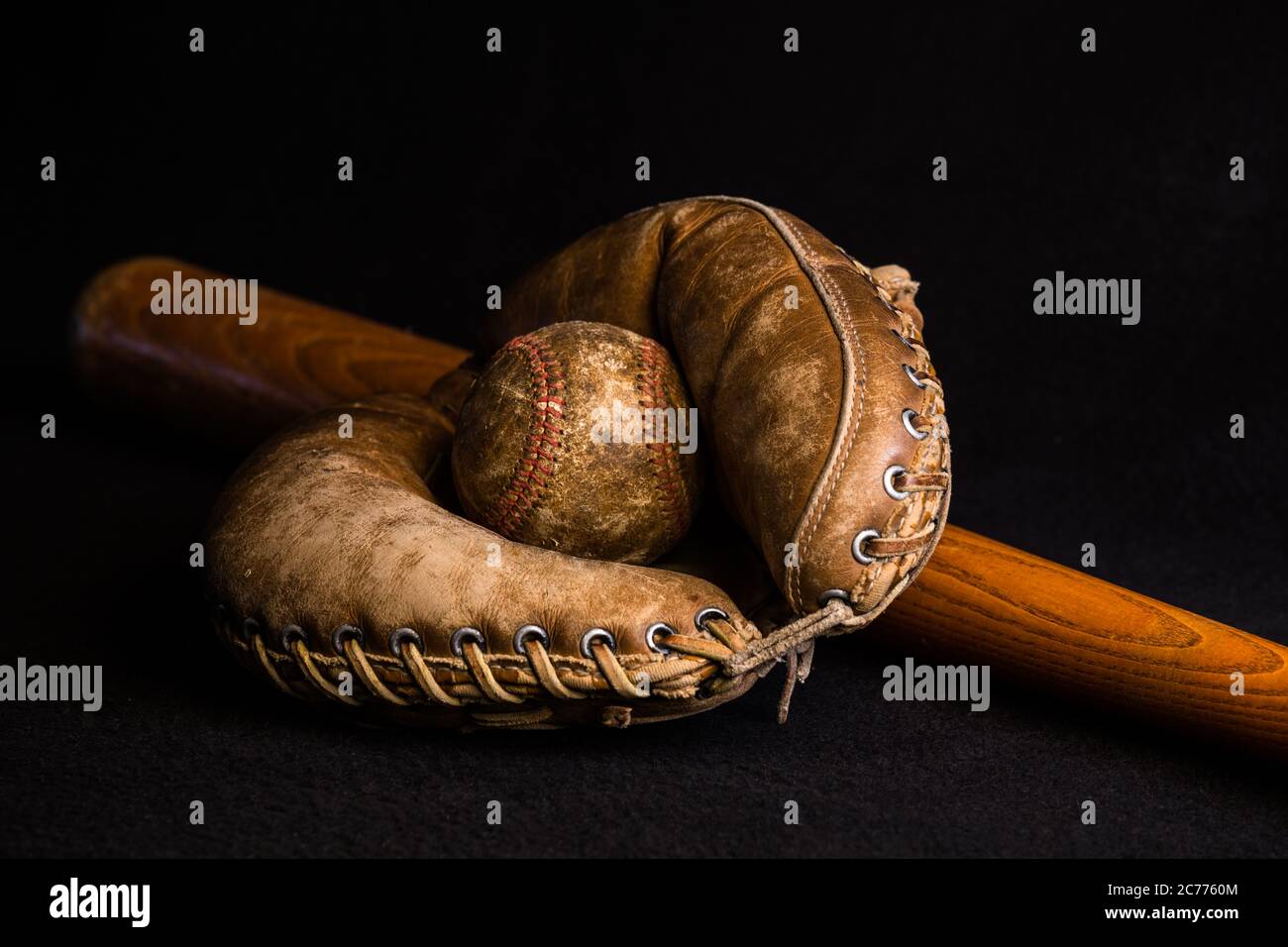 Antique catcher's mitt holding a baseball lying on an old wood bat. Stock Photo