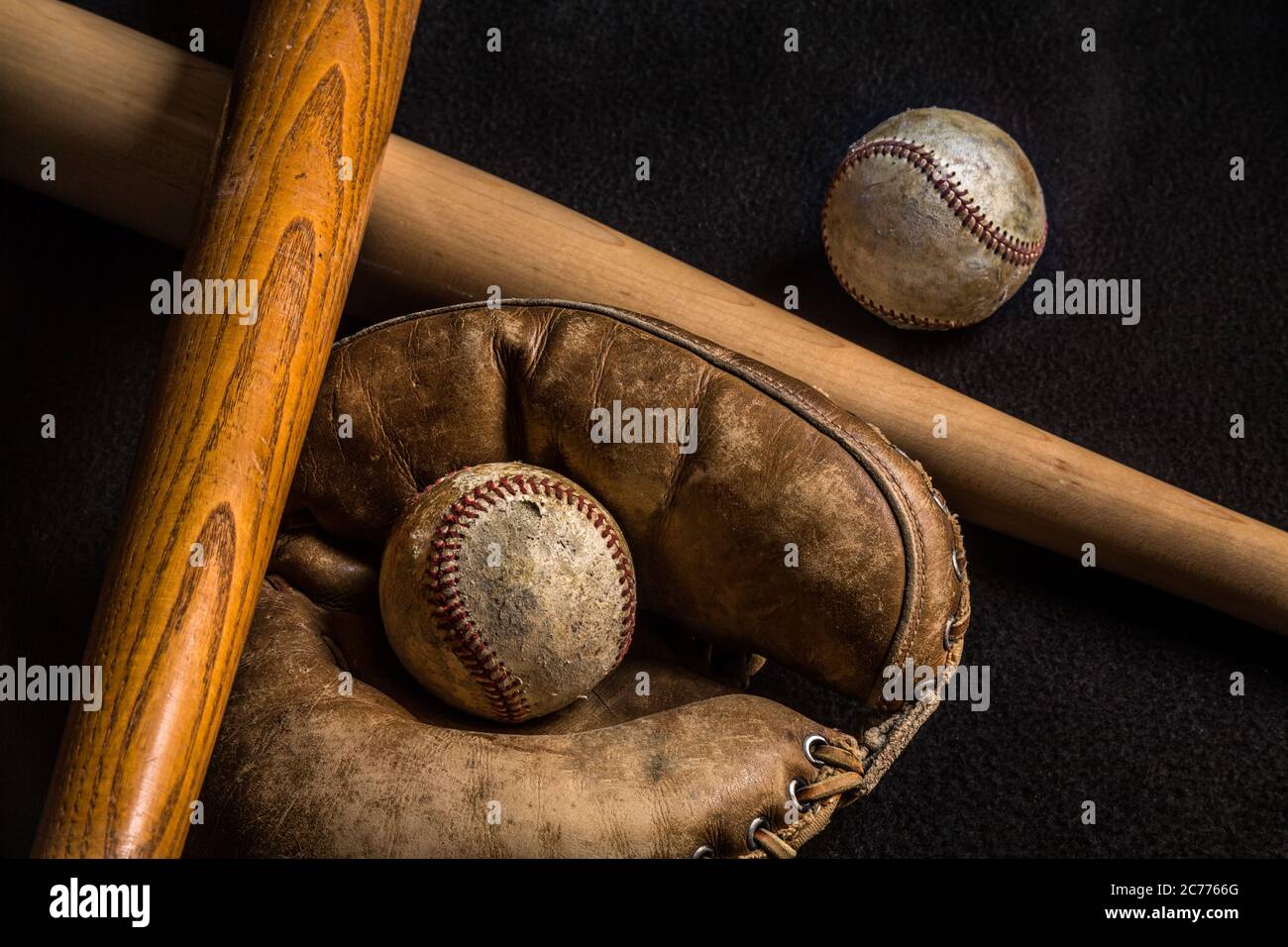 Two baseballs and a glove along with an old and new baseball bat. All but the new bat is scratched and worn from years of love of the game. Stock Photo