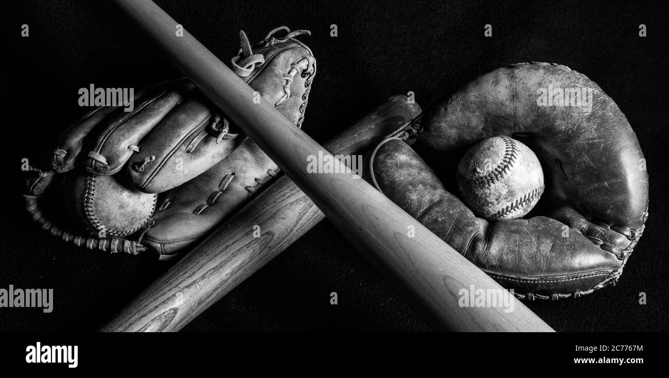Dark black and white image of old baseball gear that has been well loved. Scratched, scuffed and peeling from years of play. Stock Photo