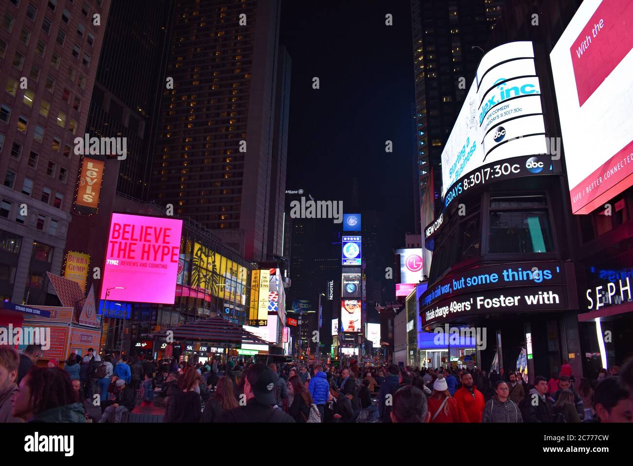 Times Square at night time.  LED advertising screens are shining brightly and the square is packed with tourists and people. Stock Photo