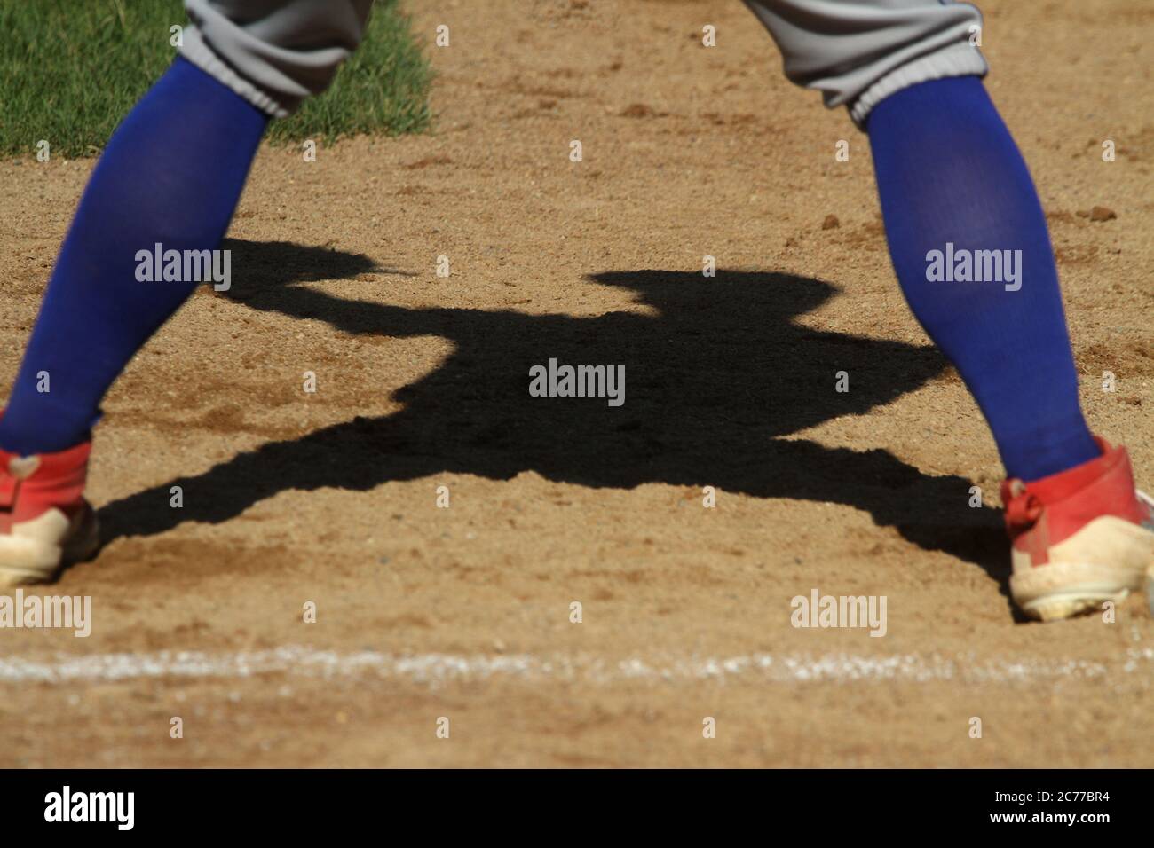 A baseball first baseman casts a shadow while covering the base for a pickoff play. Stock Photo