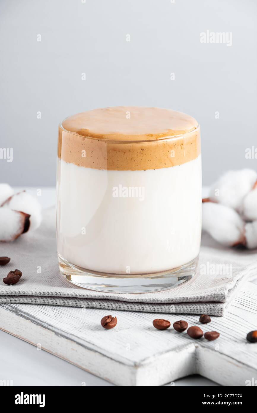 Trending Korean drink - dalgona coffee. A glass of iced milk with sweet whipped foam on a light background. Vertical photo Stock Photo