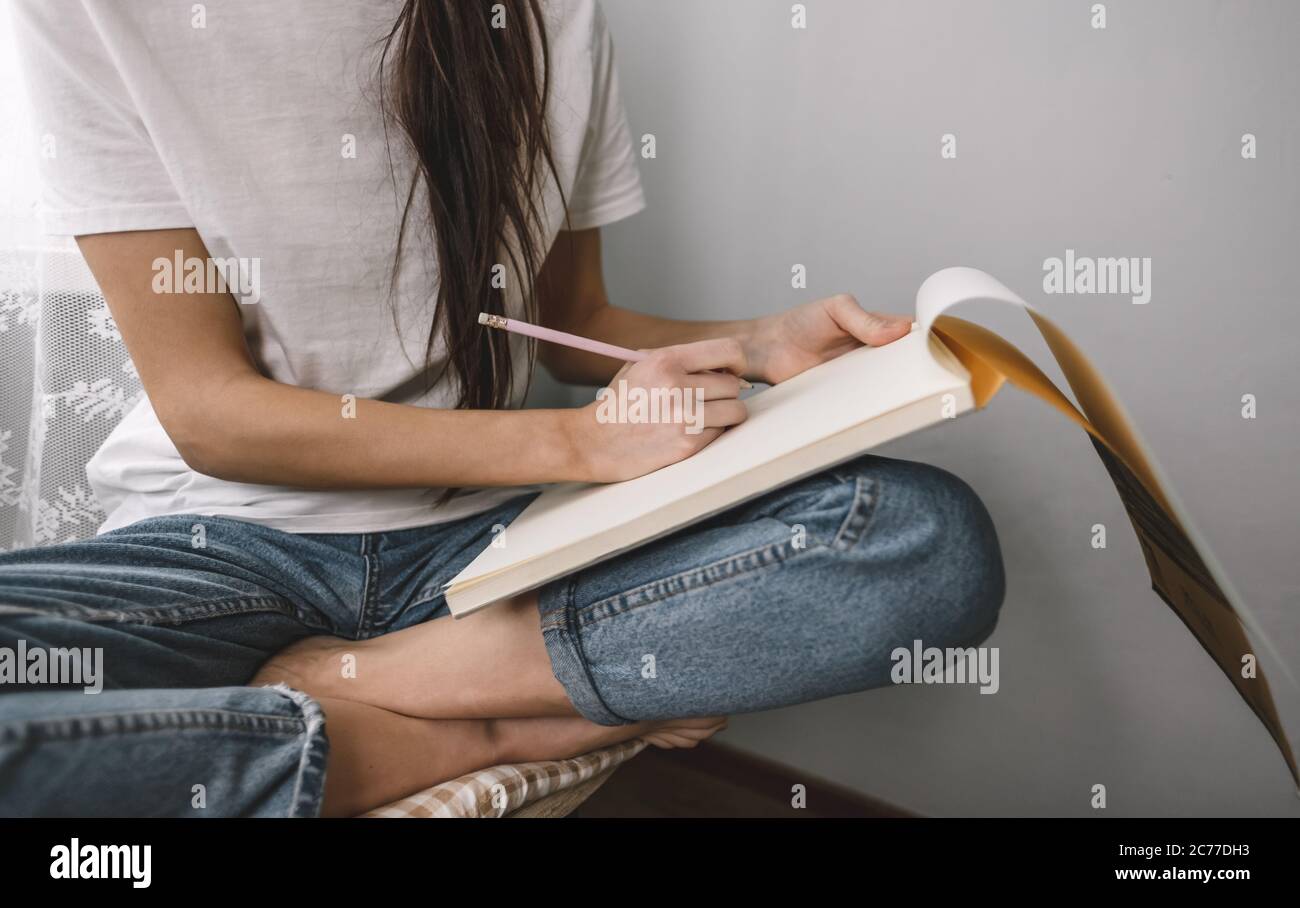 Woman artist draws in a sketchbook at home near the window, sitting on a chair Stock Photo